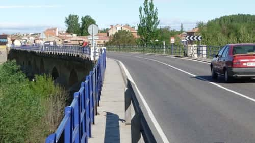 A foto mostra a ponte antiga, chegando em Puente Villarente, onde há uma estreita passagem para os pedestres ao lado da via dos carros.