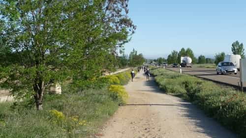 A foto da saída de Mansilla de las Mulas mostra o caminho de terra ao lado da rodovia, com vegetação ao lado.