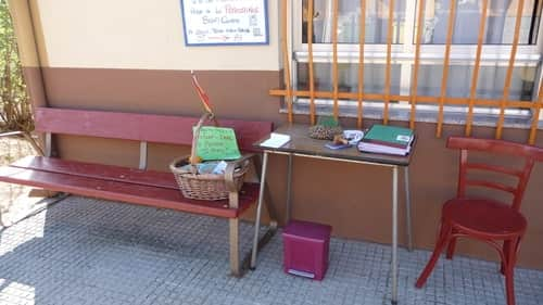 A foto mostra um banco com uma cesta em cima dele, contendo algumas coisa para o peregrino comer. Ao lado tem uma mesa com um carimbo e um bloco de papel e caneta, para deixarem uma mensagem para o Agapito. Ao lado da mesa, uma cadeira. Tudo isso em frente à casa do Agapito.