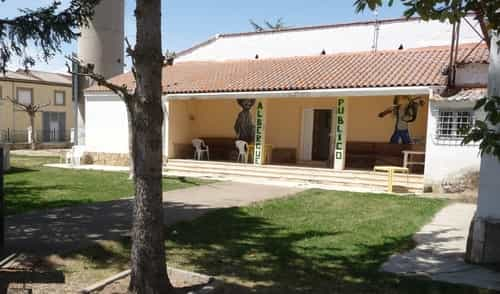 Albergue de San Martin del Camino com uma pequena varanda. Nela, um desenho de peregrinos na parede e algumas cadeiras. Na frente do albergue um gramado e uma calçada que leva até a entrada dele.