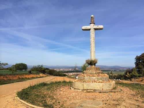 A foto mostra uma cruz de pedra e, ao fundo, as cidades de San Justo de la Vega e Astorga.