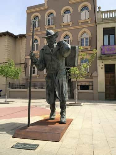 A foto mostra a escultura de um peregrino, em bronze, e o albergue Siervas de Maria, de Astorga, no fundo.