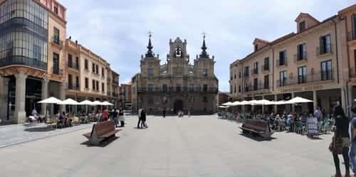 A foto mostra a prefeitura de Astorga, na praça Espanha e várias mesas com guarda-sois na frente dos bares que existem ali.