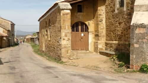 Foto da porta de entrada da igreja de Santiago, em El Ganso, com a estrada por onde os peregrinos caminham ao lado esquerdo da igreja.