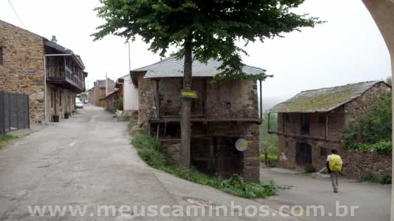 Foto do pueblo de Riego de Ambrós, mostra que o lugar é uma descida constante. Aparece um peregrino na parte de baixo da rua.
