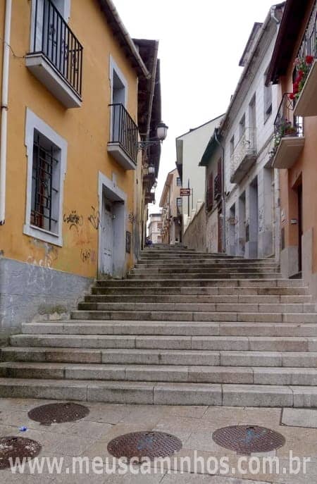 Foto da escadaria logo depois da Praça da Virgem, em Ponferrada, vista de baixo. Ao lado da escadarias há várias casas.