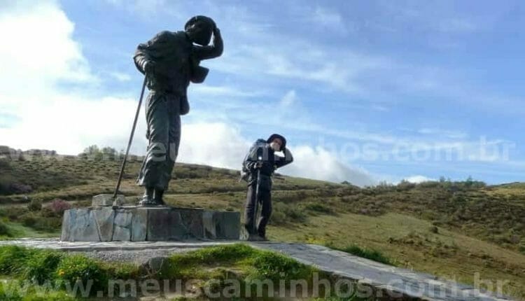 Foto da grande estátua de Sán Roque, no Alto do San Roque, no Caminho de Santiago, com um peregrino ao lado imitando a estátua.