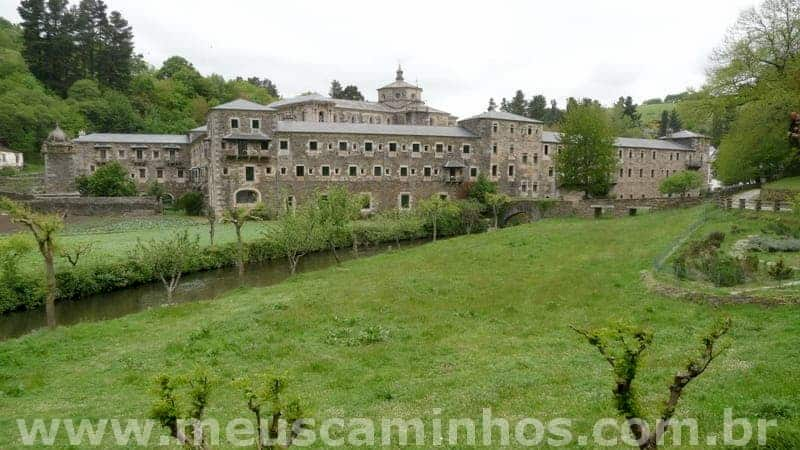 Foto do monastério de Samos. Entre o local que a foto foi tirada e o monastério há vegetação rasteira e um pequeno rio.