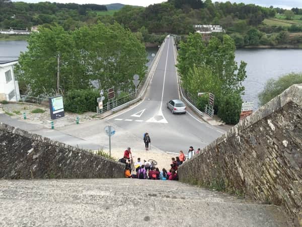 A foto, tirada da parte de cima da escadaria, mostra a escadaria e a ponte da chegada em Portomarín.